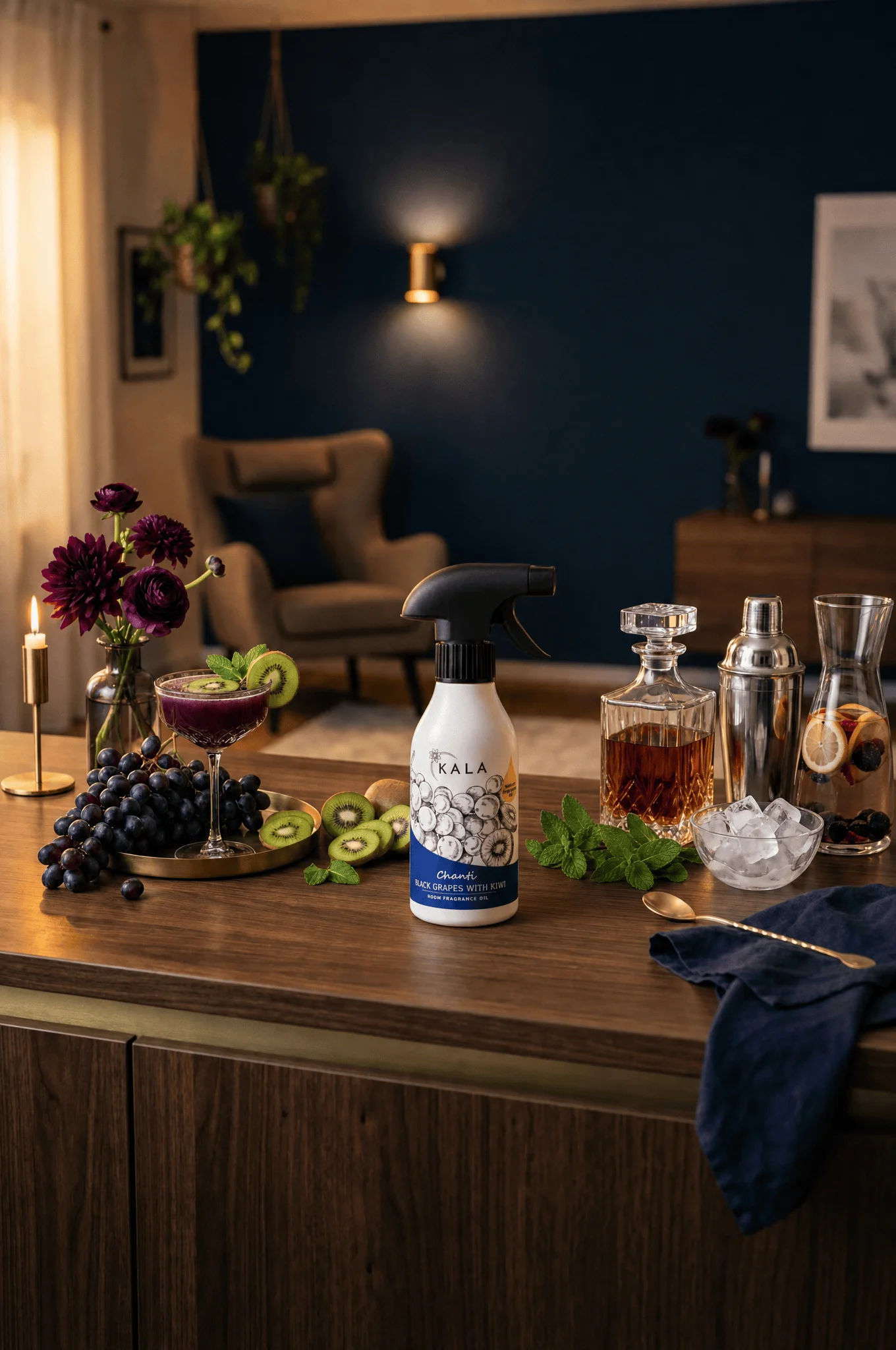 Odświeżacz powietrza KALA Black Grapes with Kiwi na drewnianym stole w salonie z koktajlami, winogronami i kwiatami.
